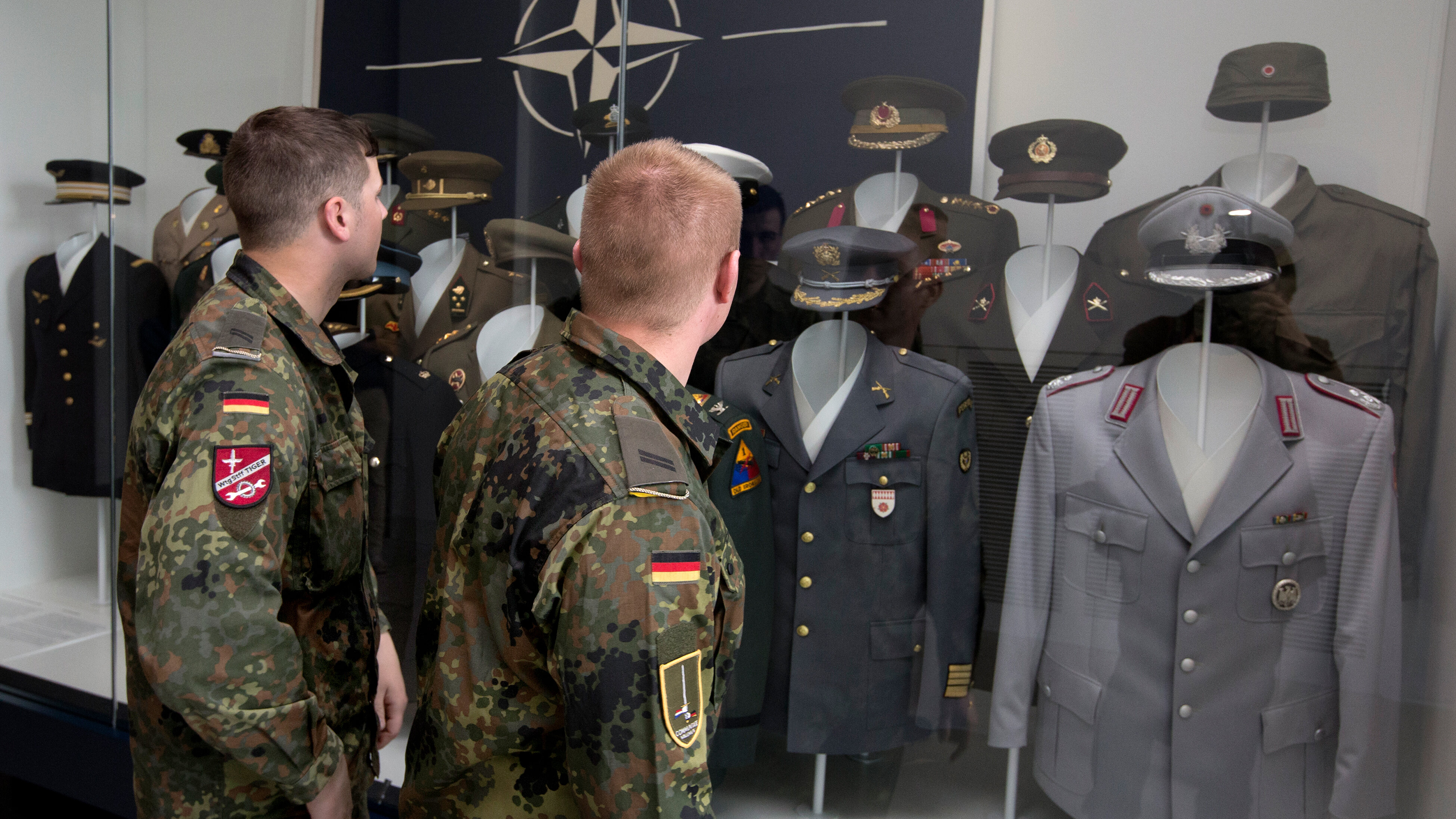 Das Bild zeigt zwei Soldaten vor einer Vitrine mit Nato-Uniformen.