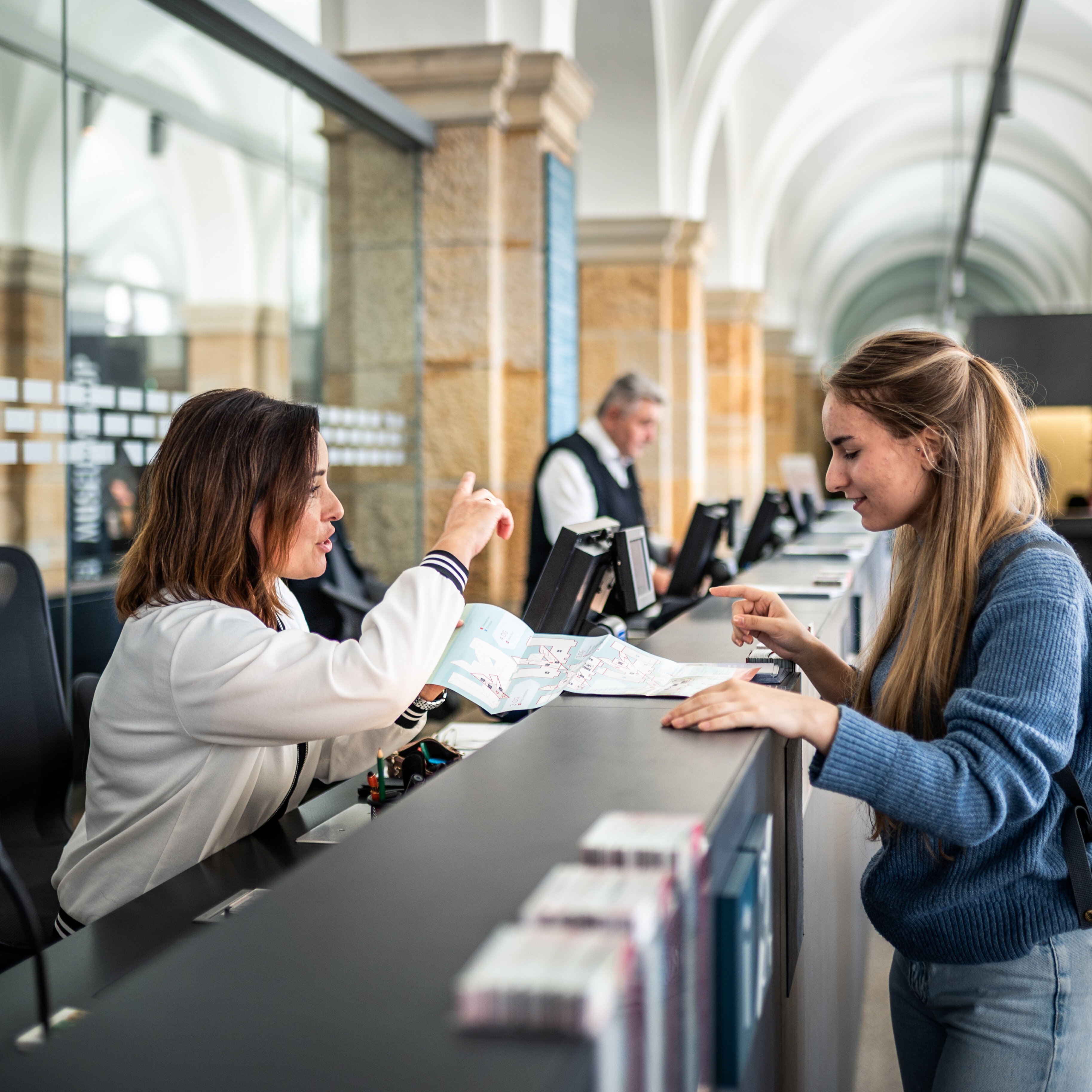 Eine Mitarbeiterin des Museums an der Kasse erklärt einer Besucherin den Lageplan der Ausstellung. 