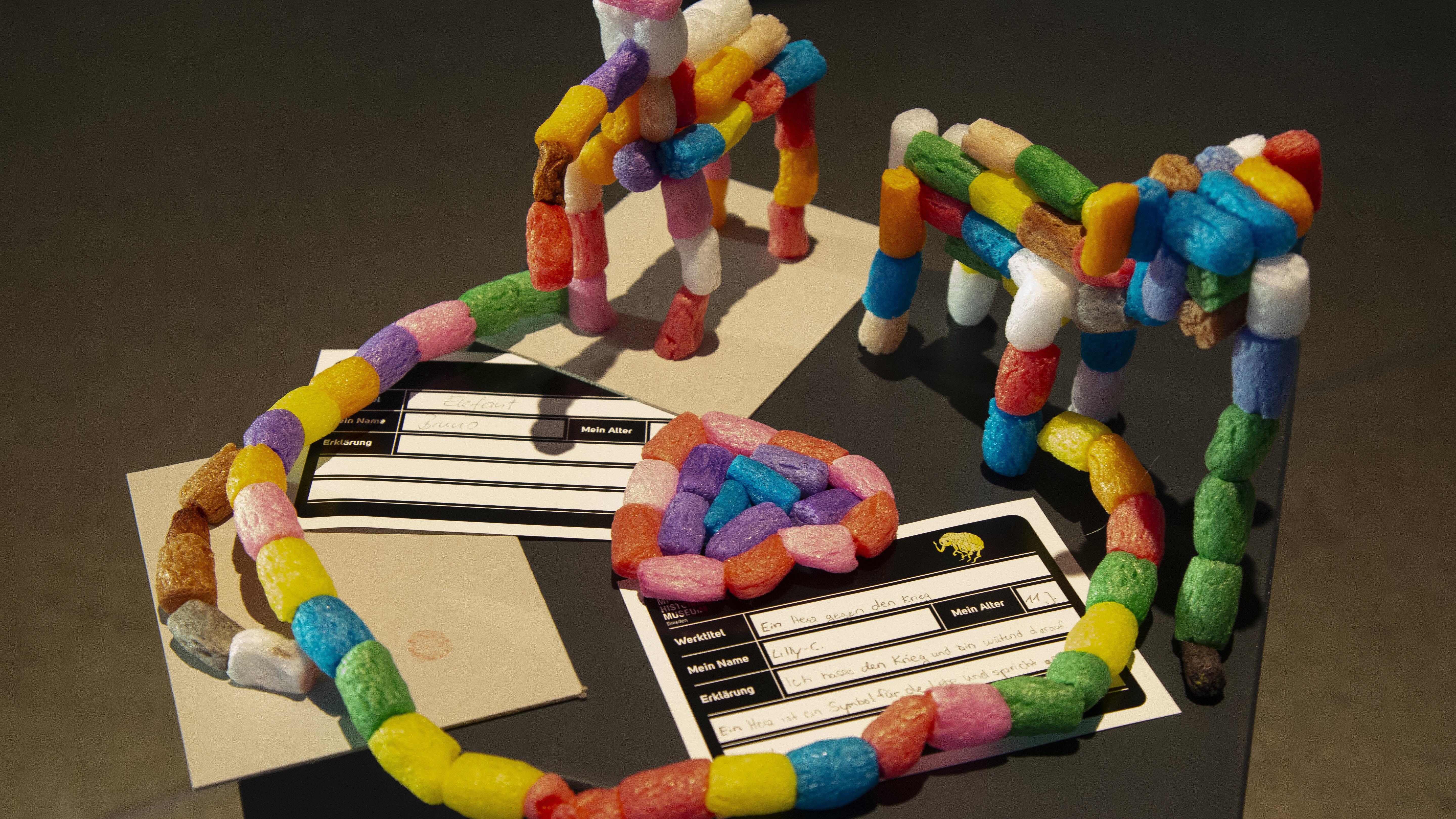 Auf einem schwarzen Podest stehen bunte Figuren, die Kinder aus FischerTiPs-Elementen zusammengefügt haben.  