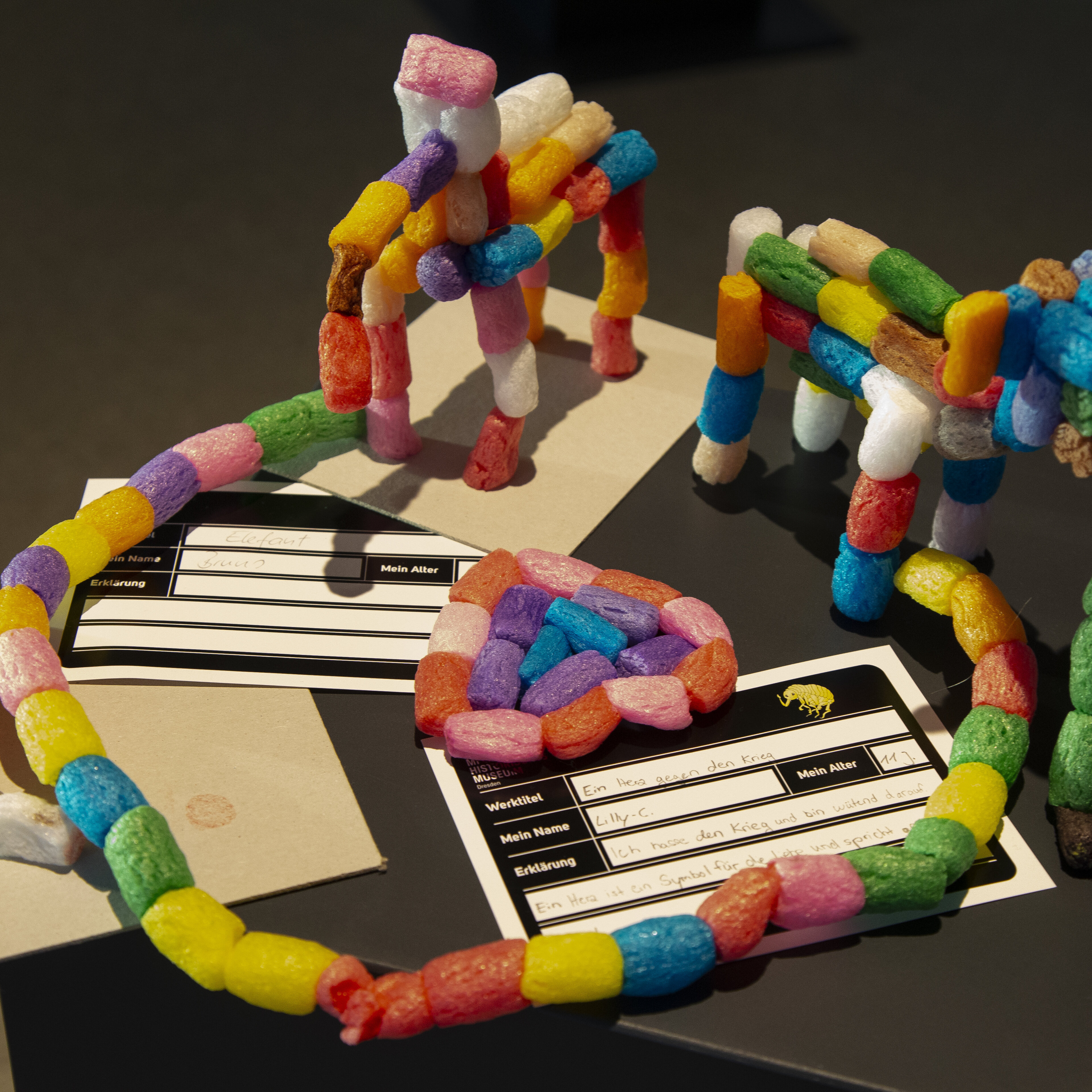 Auf einem schwarzen Podest stehen bunte Figuren, die Kinder aus FischerTiPs-Elementen zusammengefügt haben.  