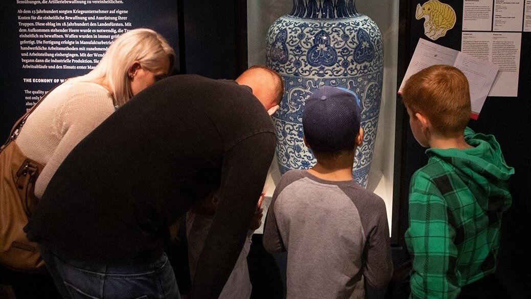 Eine Familie mit drei Kindern betrachtet gemeinsam eine große, weiß-blaue chinesische Vase in einer Vitrine.  