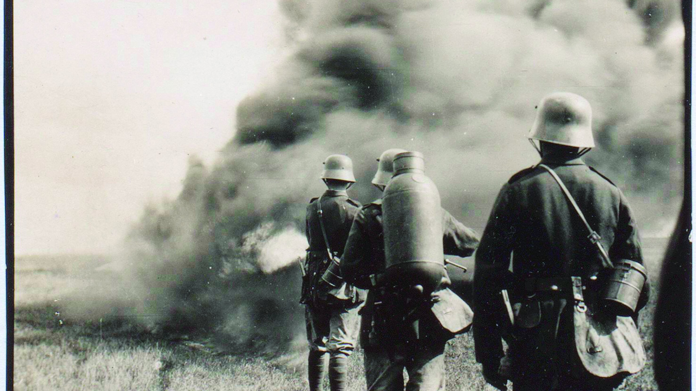 Das Schwarzweißfoto zeigt drei deutsche Soldaten im Ersten Weltkrieg mit Stahlhelm und tragbarem Flammenwerfer „Kleif“. 
