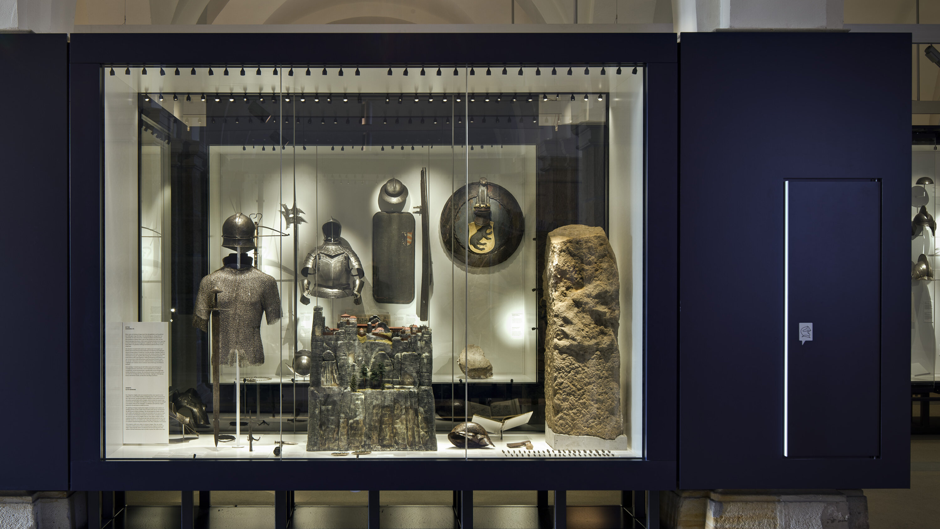 Das Bild zeigt eine Vitrine mit mittelalterlicher Ausrüstung sowie dem Modell einer Burg. 