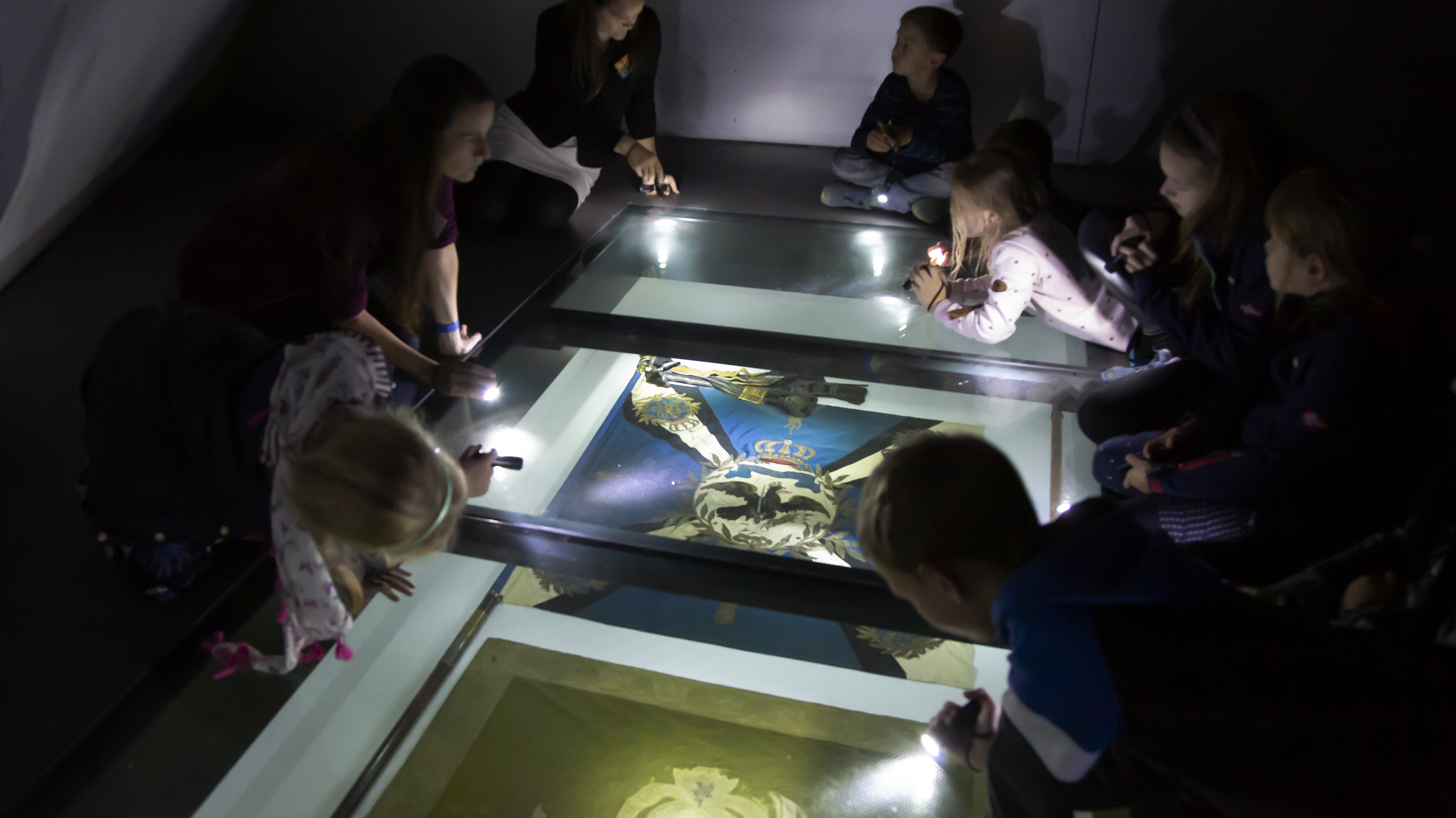 Kinder leuchten mit Taschenlampen zwei Fahnen im Ausstellungsbereich „Formation der Körper“ an. 