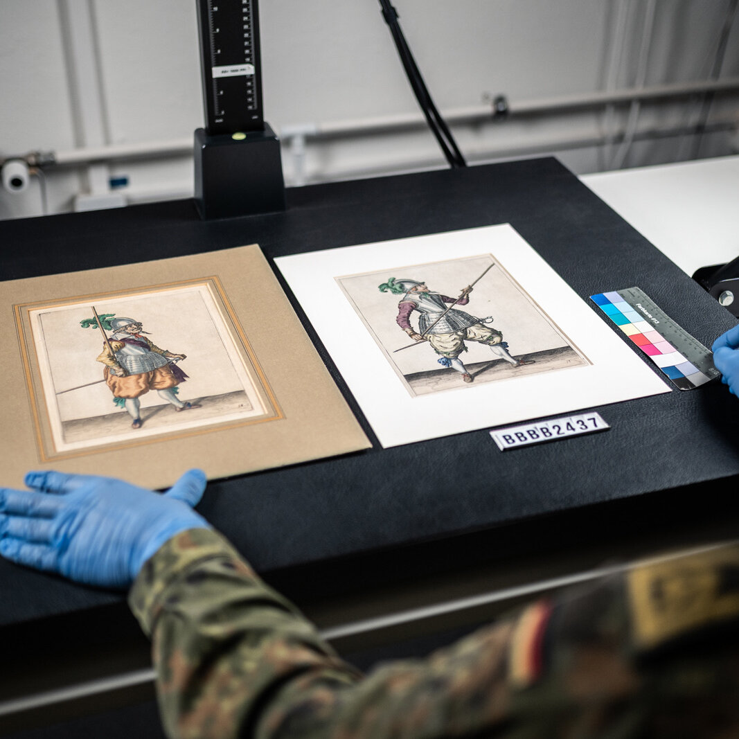 Auf dem Bild ist zu sehen, wie Grafiken auf einem Scanner bereitgelegt werden, um sie zu digitalisieren. 