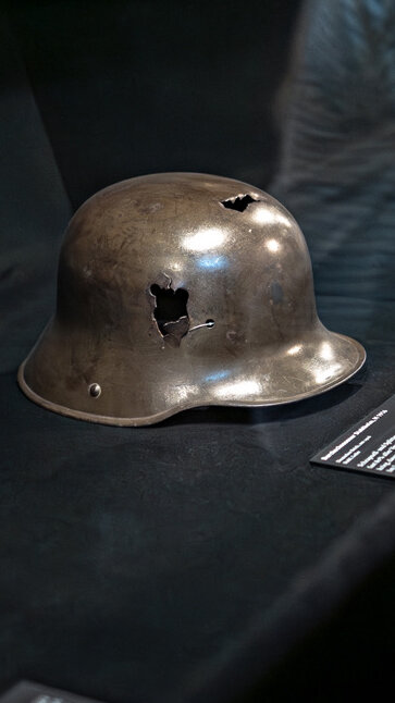 Das Bild zeigt, wie Gäste den Sichtschutz vor den Vitrinen im Bereich Leiden am Krieg öffnen. 