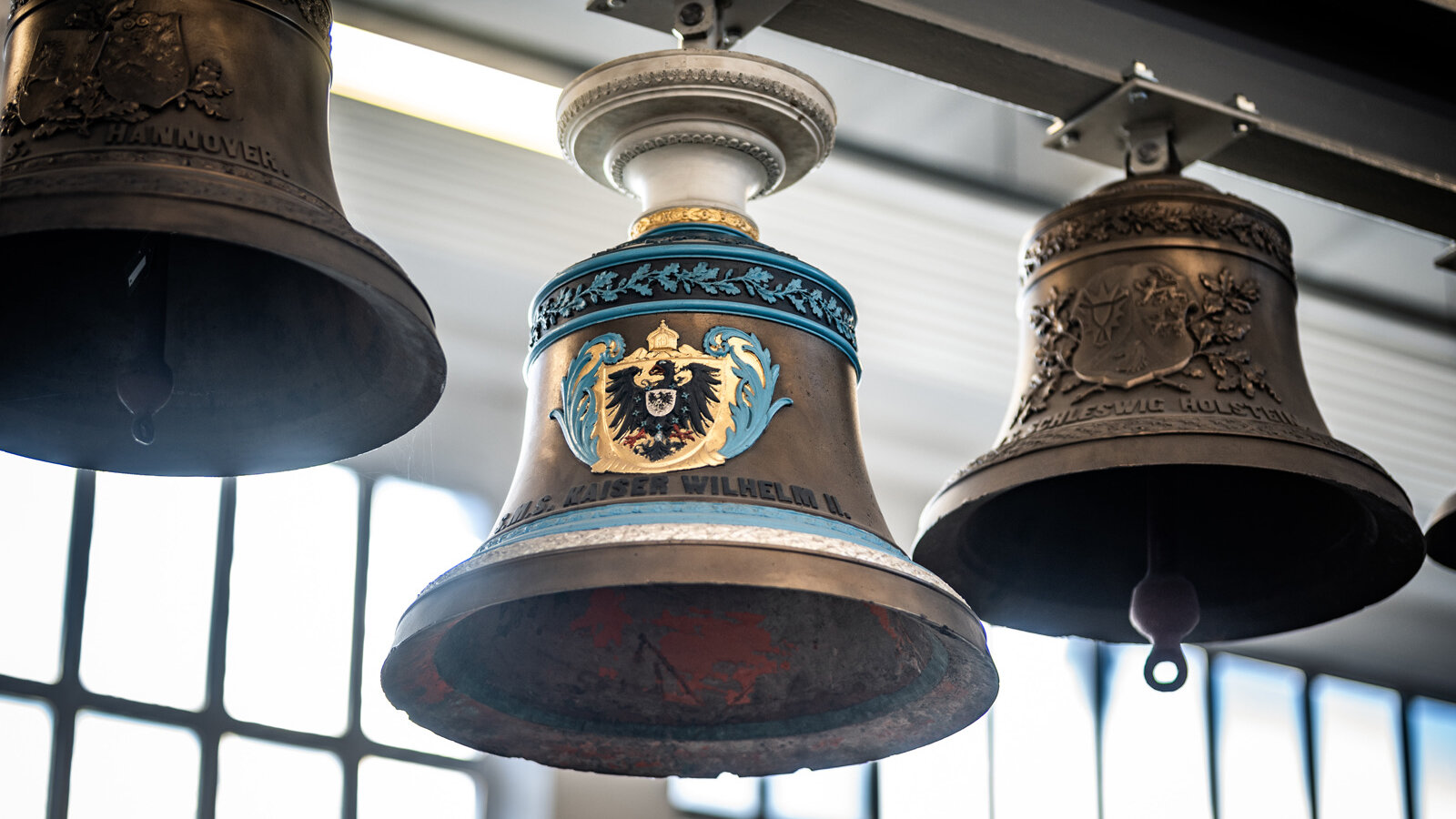 Four suspended ship’s bells bearing emblems and engravings. 