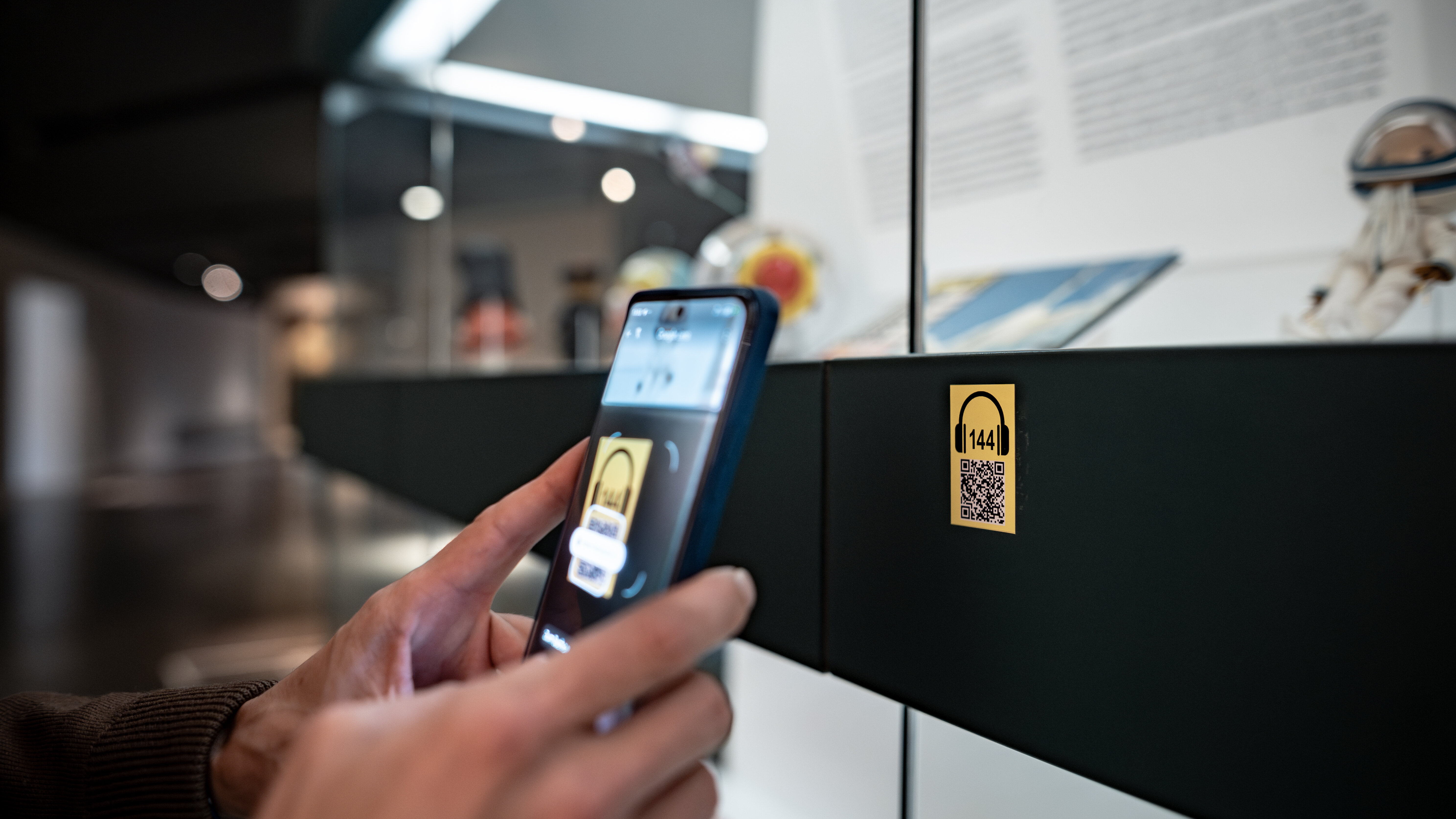Das Bild zeigt, wie ein QR-Code mit dem Smartphone aufgerufen wird, um eine Exponaterklärung anzuhören. 