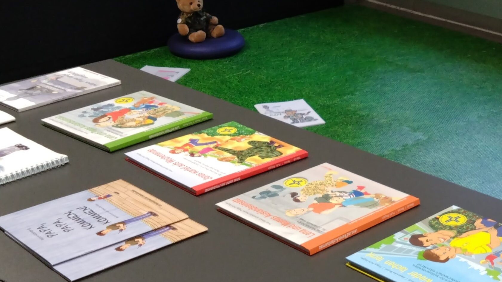 Auf einem Tisch in der Bibliothek liegen Kinderbücher. Im Hintergrund ist ein Teddybär in Bundeswehr-Tarnuniform zu sehen. 
