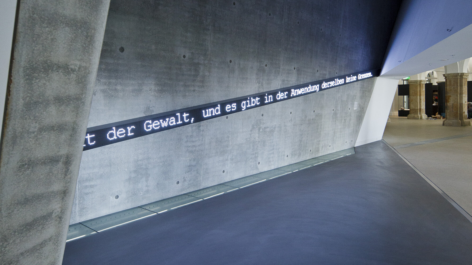 Auf einer Sichtbetonwand steht in Leuchtschrift ein Clausewitz-Zitat: „Der Krieg ist nicht Menschenfreundliches“.