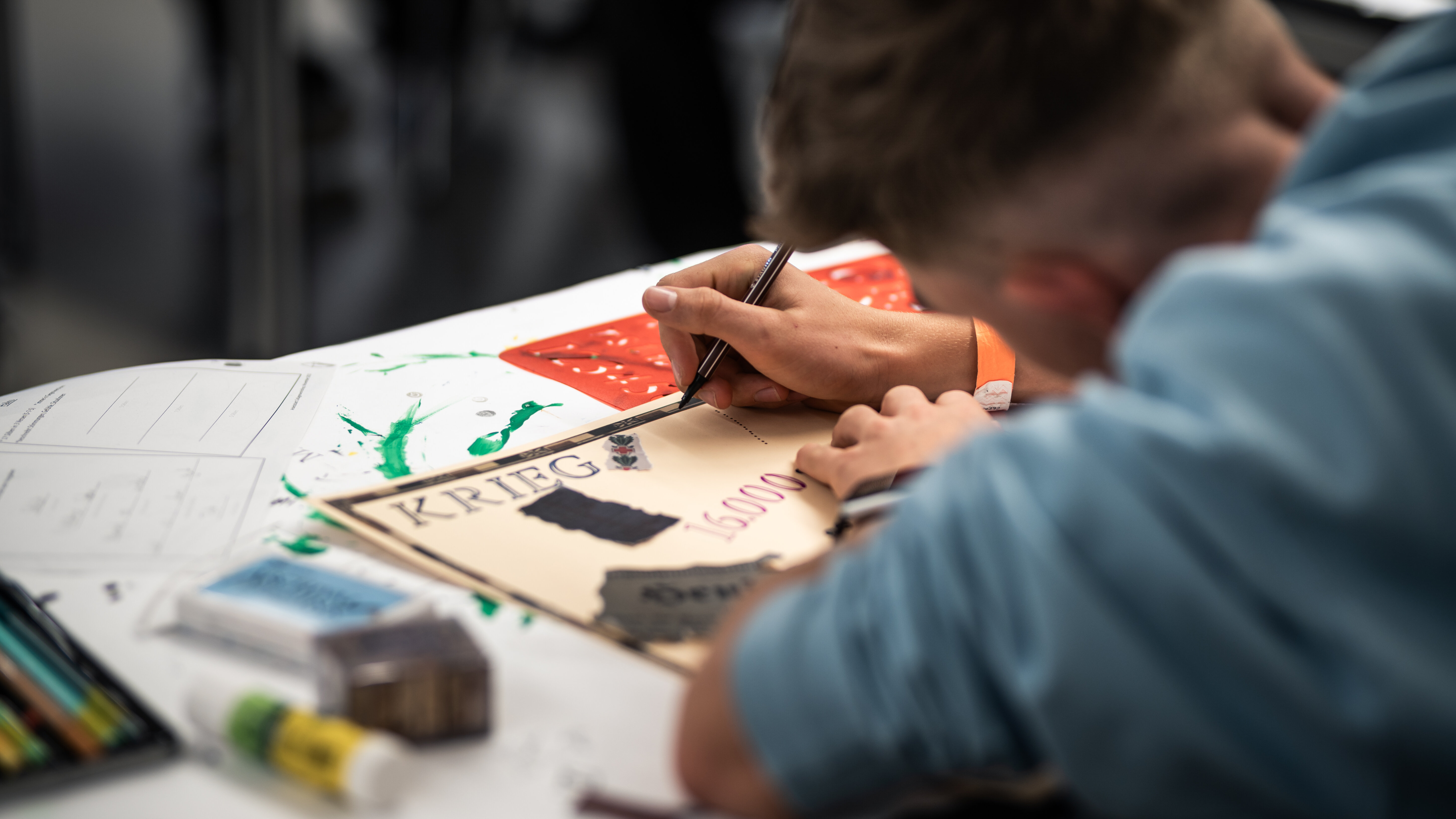 Ein Jugendlicher arbeitet an einer Collage. Auf dem Tisch liegen Leimstift, Schablonen und Stempel. 