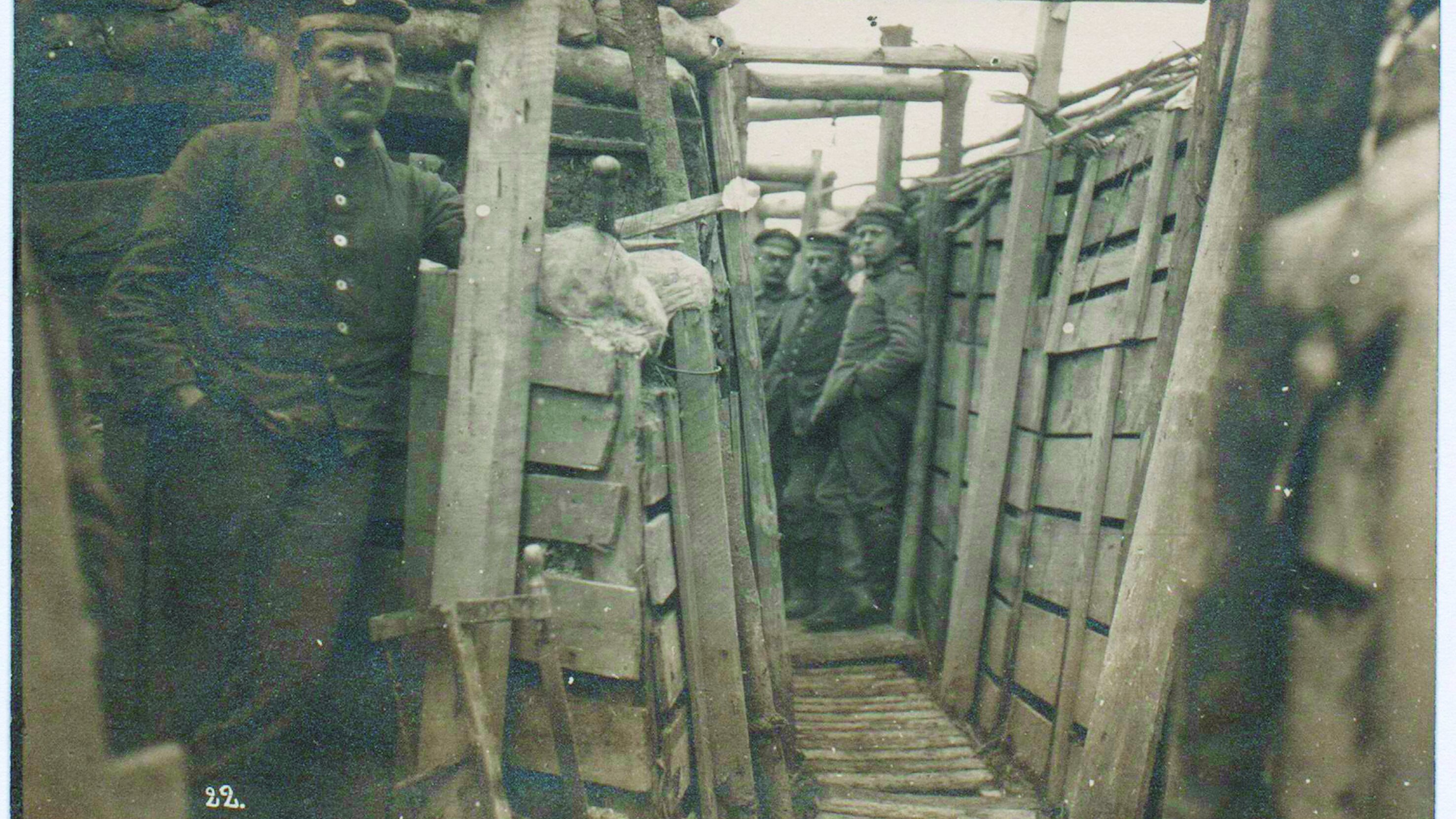 Die schwarz-weiße Fotopostkarte zeigt vier deutsche Soldaten, die in lässiger Haltung in einem Schützengraben stehen. 